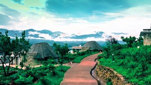 A pathway leading to traditional-style huts surrounded by lush greenery and mountains in the background. - Halala Kella Eco Lodge (Zima)