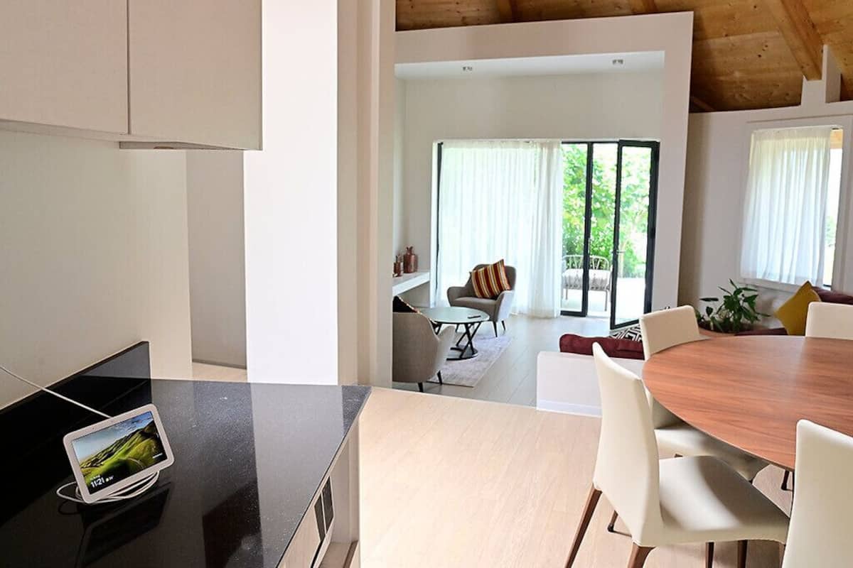 A modern kitchen with a black countertop and a tablet. There is a dining area with a wooden table and white chairs.