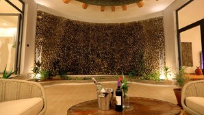 A circular seating area with a stone wall backdrop, a bottle of wine, and a wine glass on a wooden table. - Halala Kella Eco Lodge (Zima)