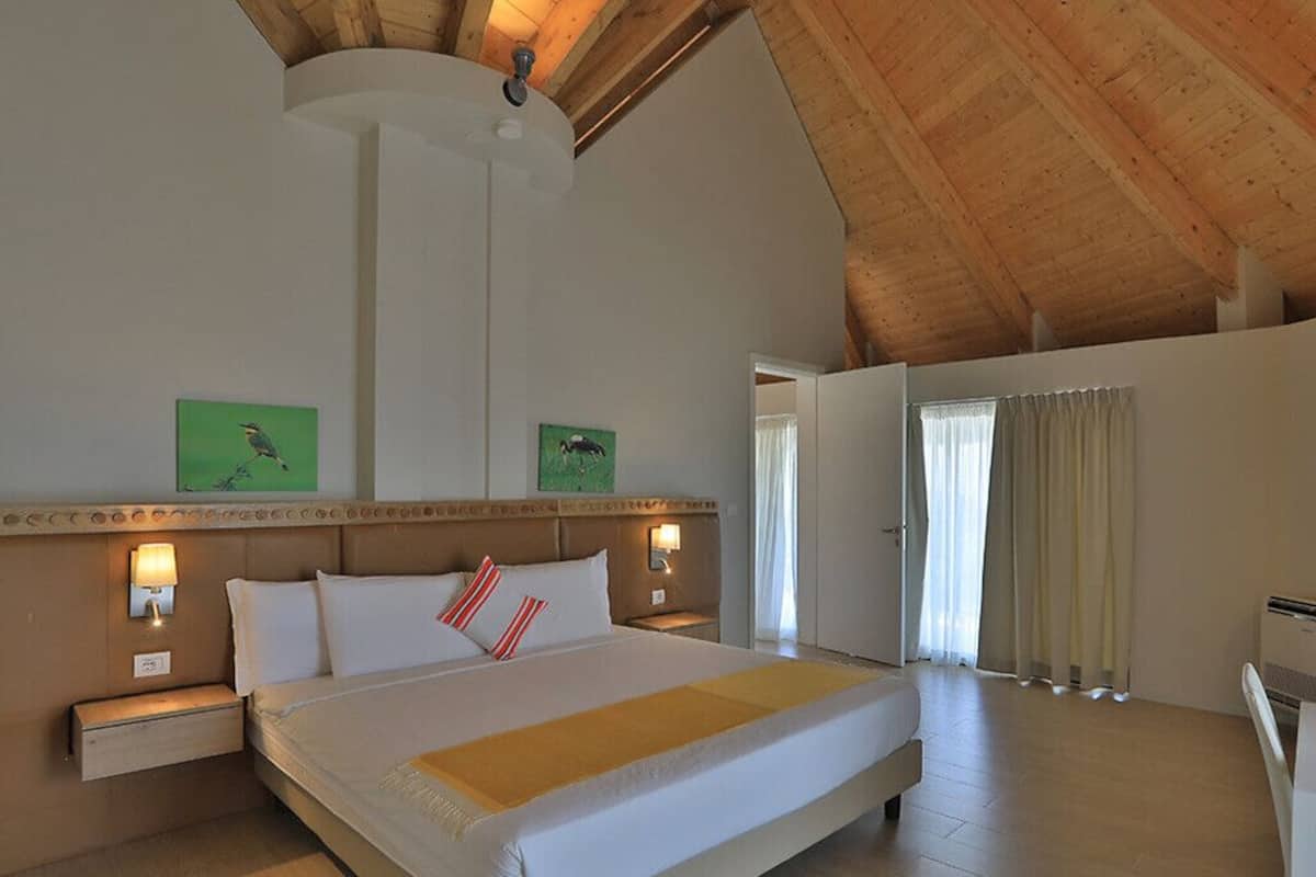 A bedroom with a large bed, wooden ceiling, and two wall-mounted lamps.