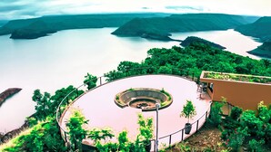 A circular observation deck with a central viewing area, surrounded by lush greenery and overlooking a large body of water with distant landforms. - Halala Kella Eco Lodge (Zima)