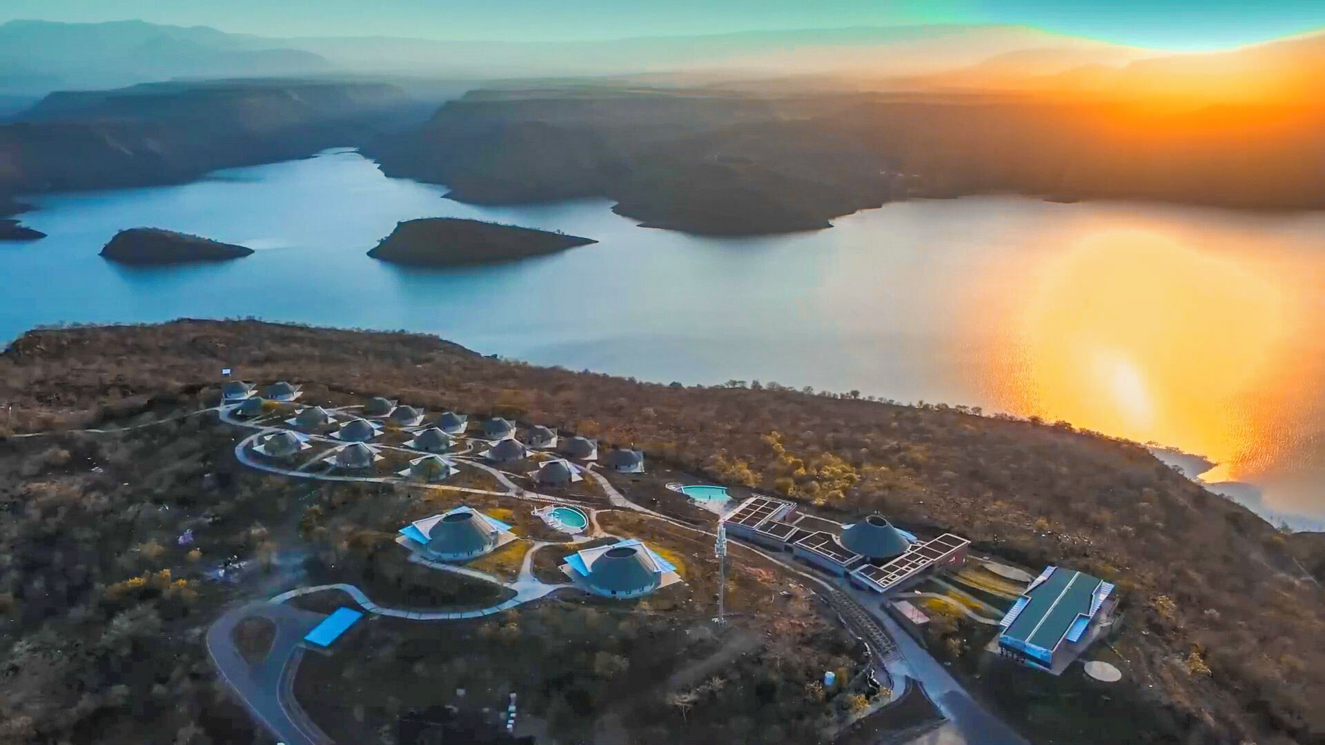 An aerial view of a resort with multiple dome-shaped buildings, a swimming pool, and a winding road.