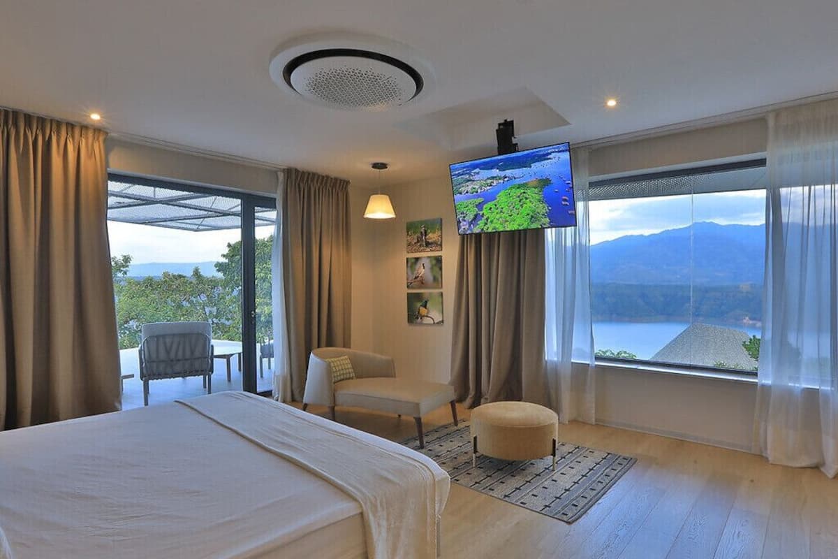 A hotel room with a bed, a TV, a chair, and a view of mountains.