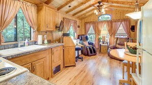 A cabin interior with wooden walls and floors, a kitchen area with granite countertops, a dining table, and a massage chair. - Hike & Fish: Cozy Cabin w/ Patio in Show Low! (Show Low)