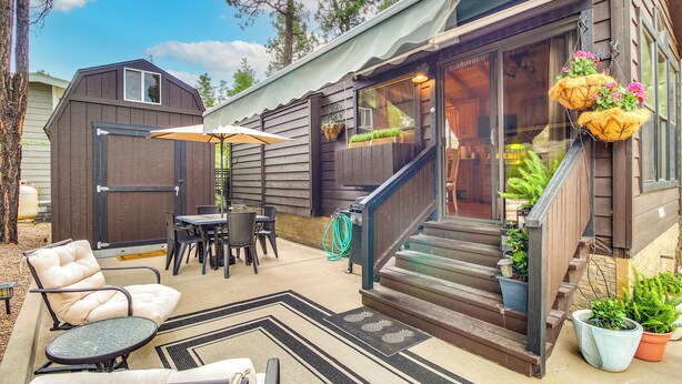 A patio with a chair, table, and umbrella, a staircase with potted plants, and a wooden fence. - Hike & Fish: Cozy Cabin w/ Patio in Show Low! (Show Low)