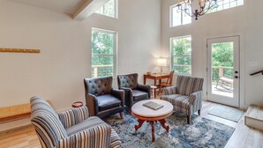 A spacious living room with leather armchairs, a striped sofa, a round coffee table, and a chandelier. Large windows provide natural light and views of the outdoors. - Views on 12 Acres: Ozark Mountain Cabin! (Parthenon)