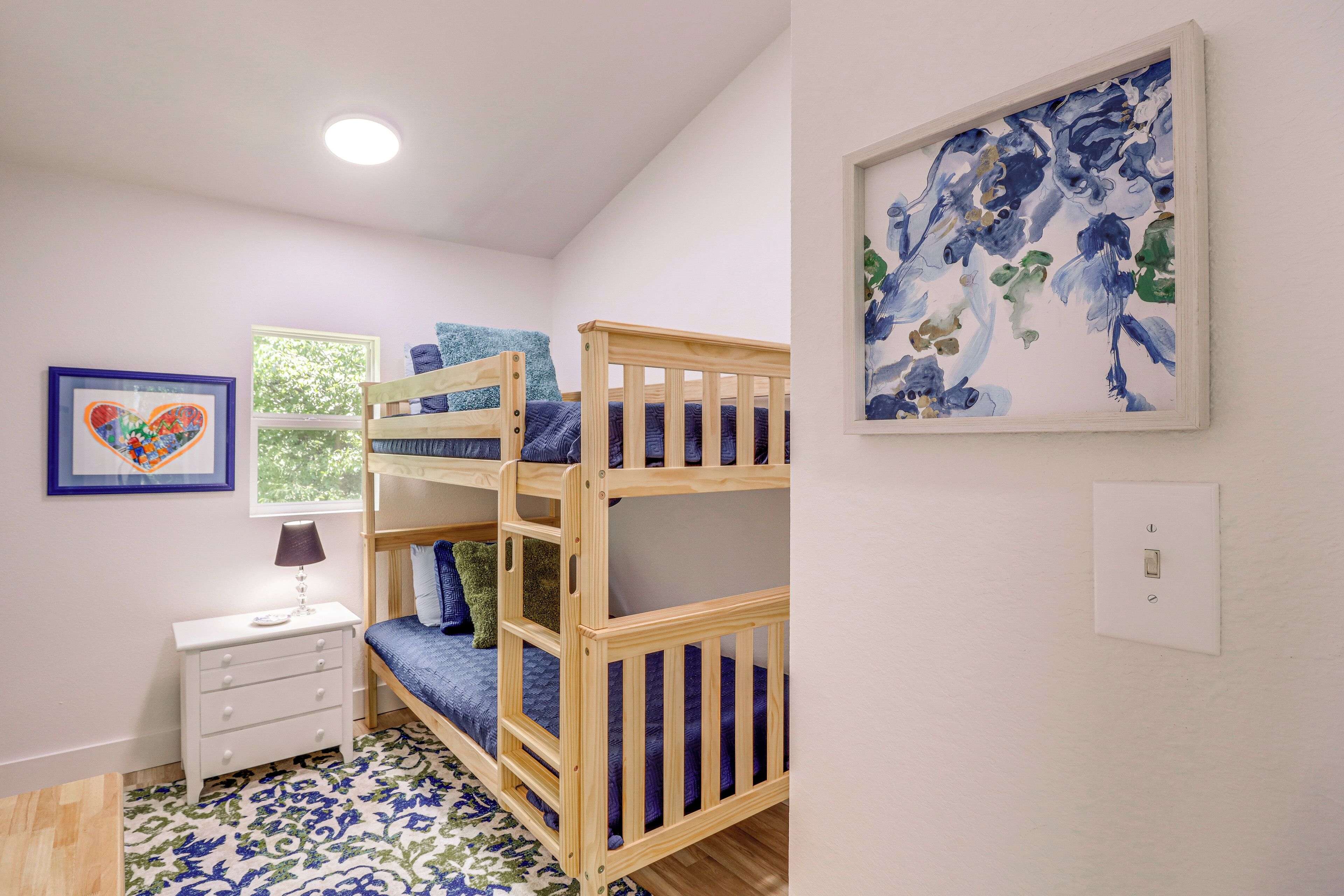 A bunk bed room with a small bedside table, a framed picture, and a window.