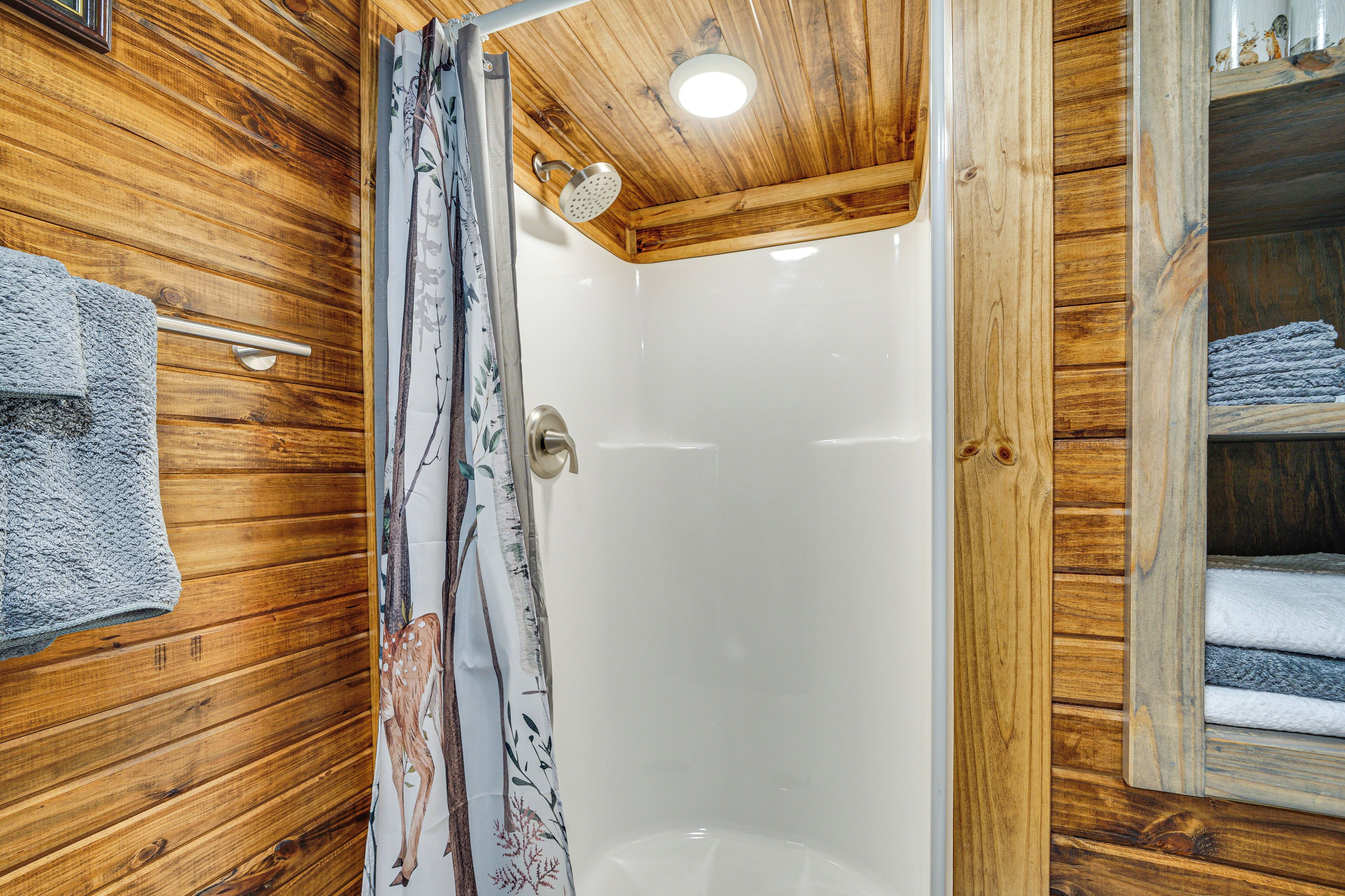 Un interior de madera con cabina de ducha de vidrio, un perchero y una repisa con toallas dobladas.