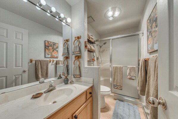 Une salle de bain avec un lavabo blanc, un miroir et un porte-serviettes. On y trouve également une zone de douche avec une porte en verre et un porte-serviettes.