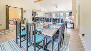 A spacious dining area with a long table, multiple chairs, and a kitchen in the background. - Waterfront Lake Anna Home: Summer Family Escape! (Bumpass)