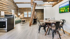 Interior de una cabaña de troncos con comedor, cocina y escalera.