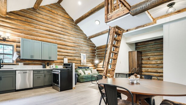 Interior de una cabaña de troncos con cocina, comedor y habitación en altillo.