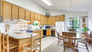A spacious kitchen with wooden cabinets, a central island with bar stools, and a dining area with a table and chairs. - Waterfront Wheeler Lake Home w/ Furnished Deck (Athens)