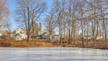 A frozen lake with leafless trees and houses in the background.