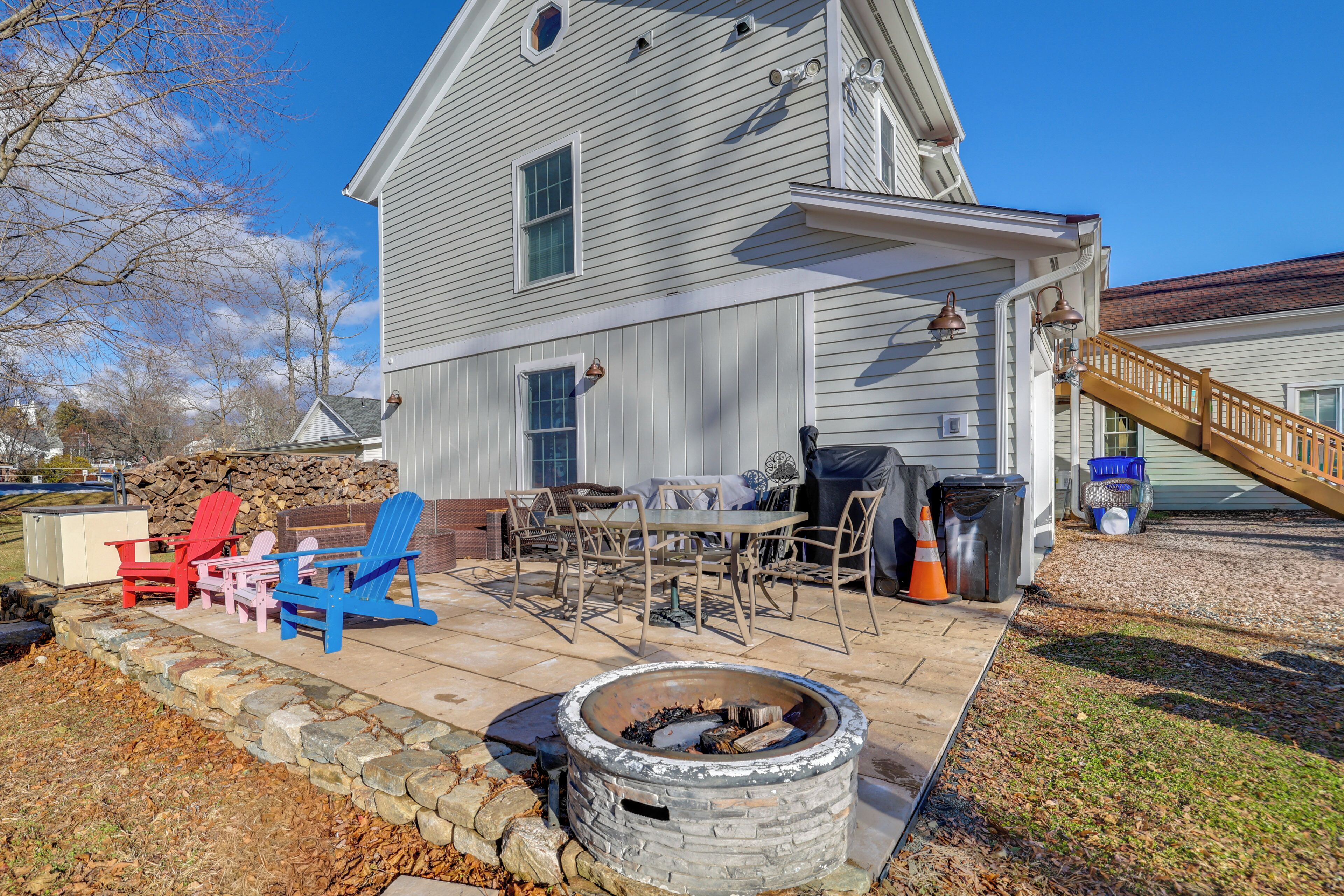 A two-story house with a patio area featuring Adirondack chairs, a fire pit, and outdoor furniture.