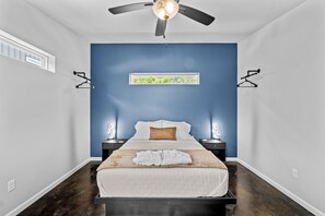 A bedroom with a bed, a ceiling fan, two bedside tables with lamps, a window, and a wall-mounted picture. - Poolside Adults-Only Escape – Hot Tub, Fire Pit Near Lake Ouachita-Home 2 (Royal)