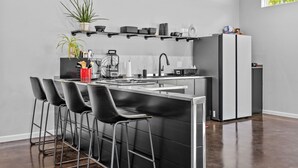 Una cucina moderna con angolo bar, sgabelli neri, un frigorifero e una pianta in vaso.