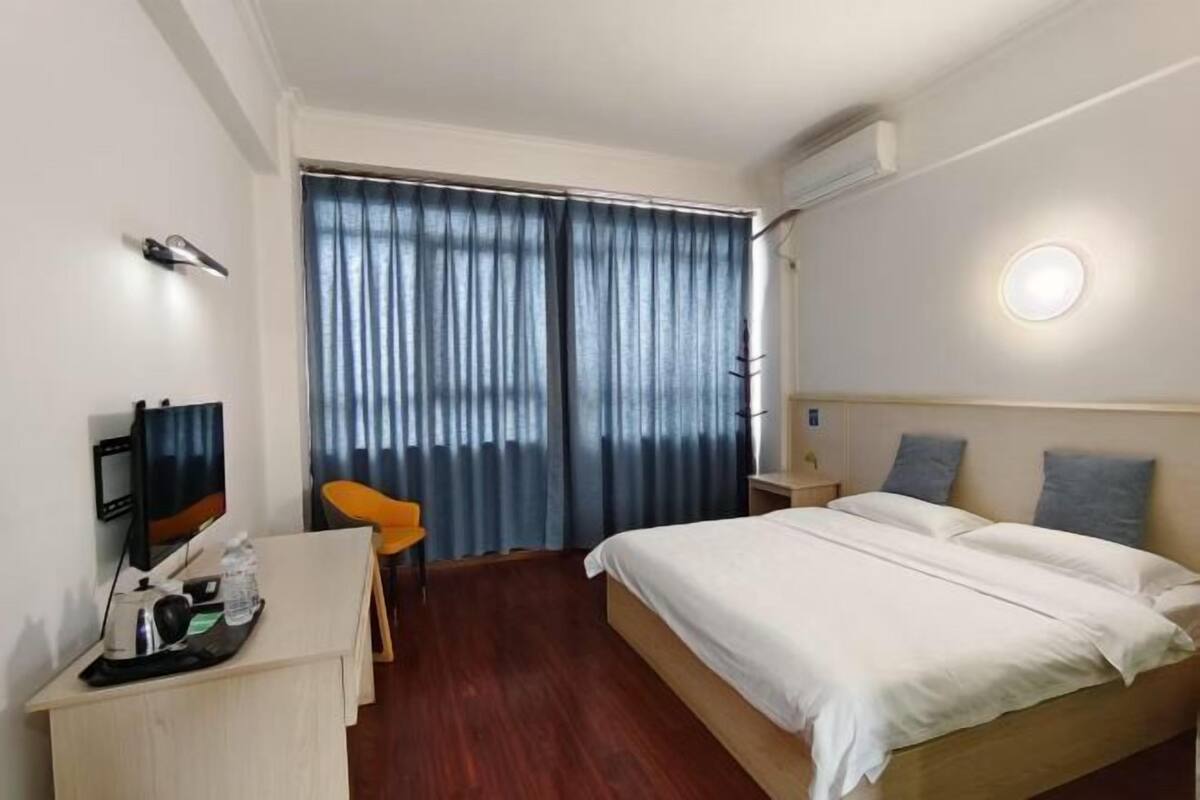 Une chambre d’hôtel avec un lit, un bureau avec un ordinateur, une chaise et une fenêtre avec des rideaux.