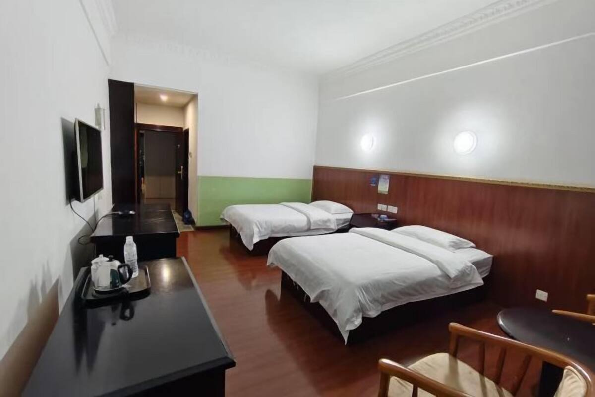 Une chambre d’hôtel avec deux lits, un bureau avec une chaise, une télévision et une petite table avec une bouteille et un verre.