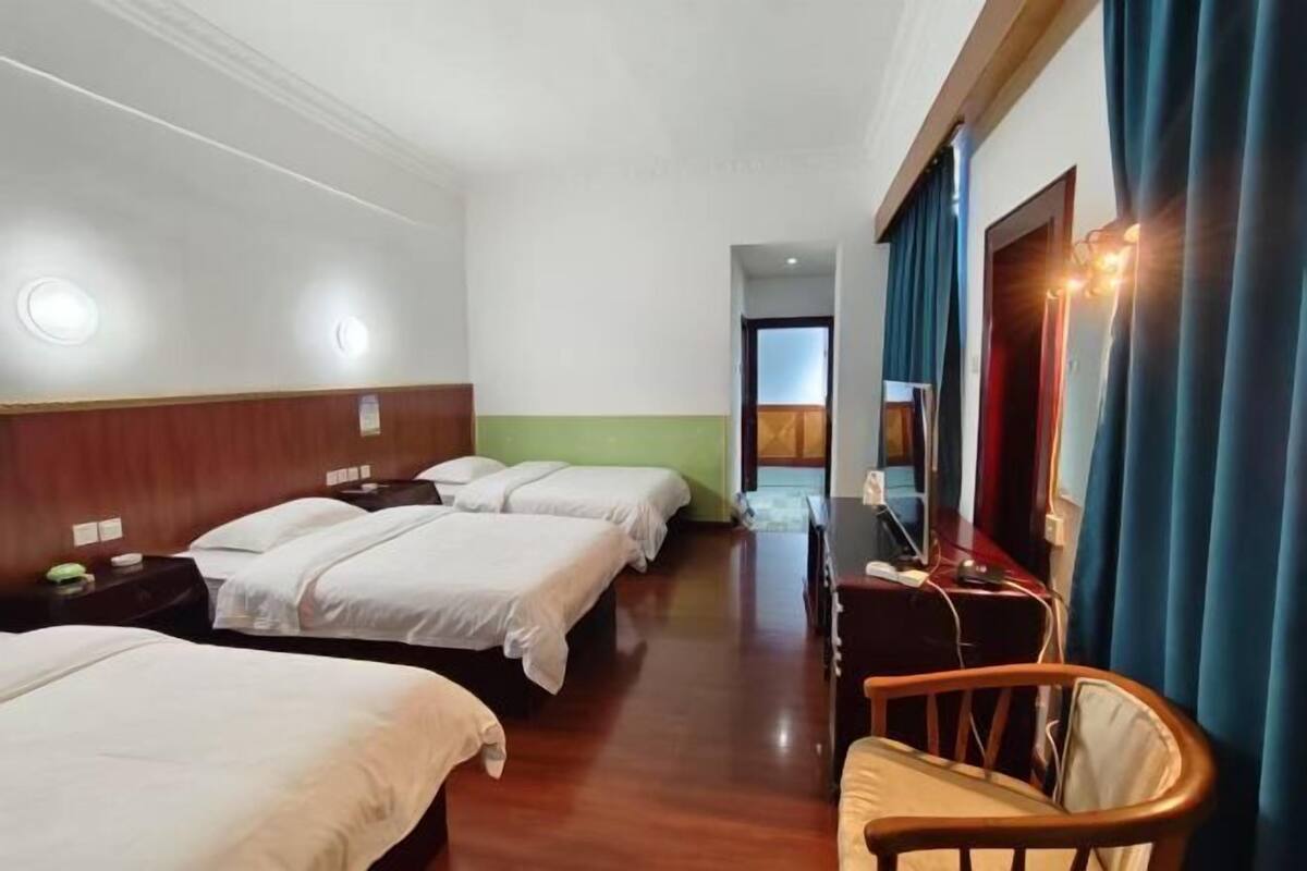 Une chambre d’hôtel avec trois lits, un bureau avec un ordinateur, une chaise et un grand miroir.