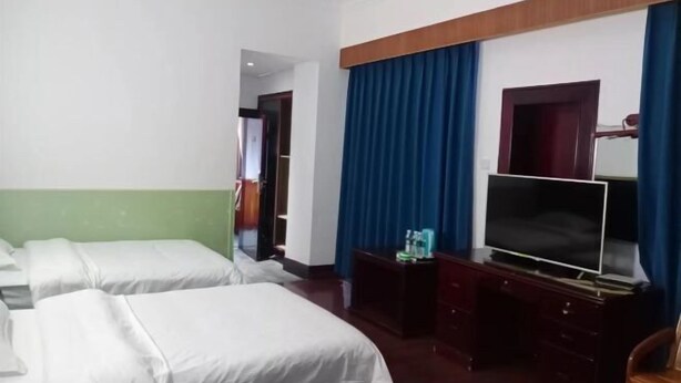 Quarto de hotel com três camas de solteiro, uma TV de tela plana, uma escrivaninha de madeira e um espelho.
