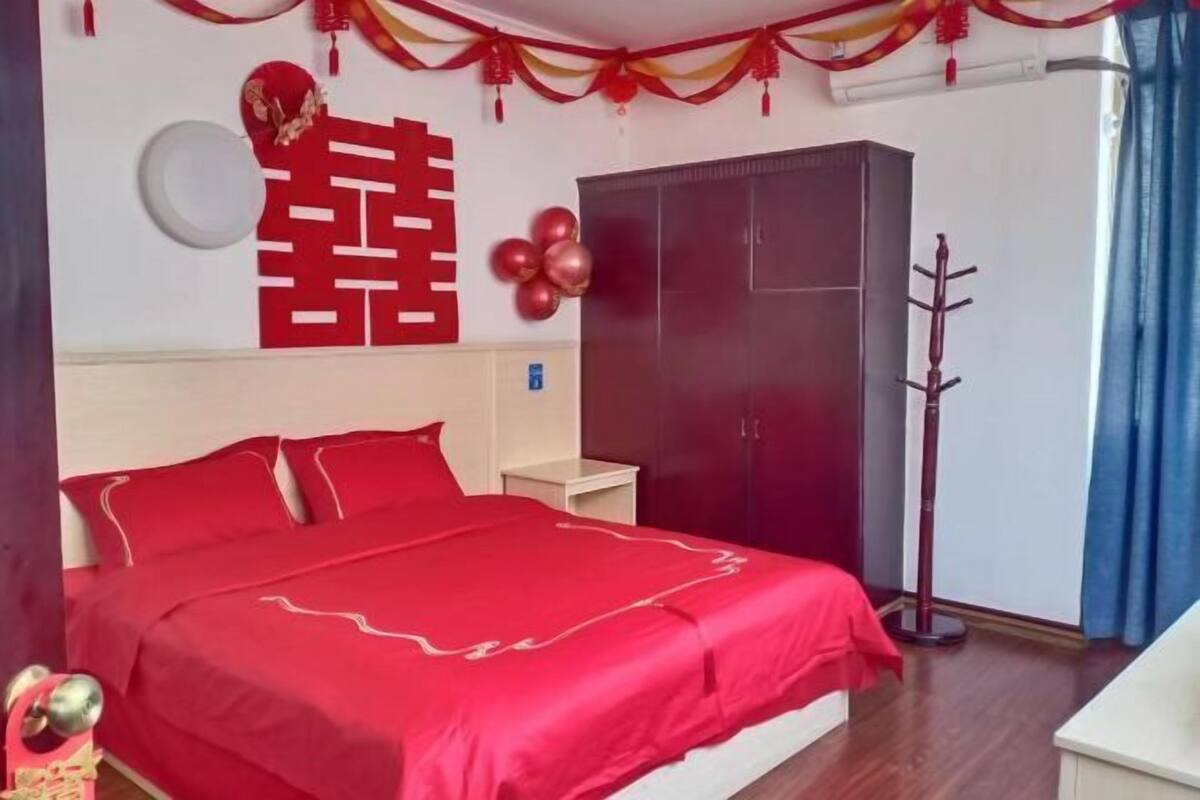 Une chambre à coucher avec une couvre-lit rouge, une armoire et un porte-manteau.