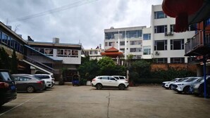 Uma área de estacionamento com vários carros, um edifício com telhado vermelho e uma escadaria que leva a um andar superior.