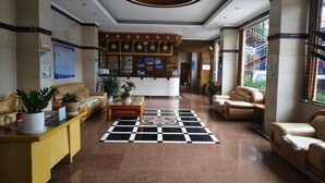 Um hall com piso xadrez, sofás de couro, um balcão de recepção e um teto decorativo.