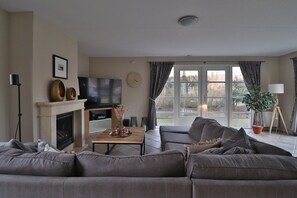 A living room with a fireplace, a television, a sofa, a coffee table, and a view through the glass doors.