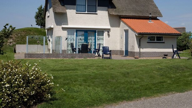 Ein zweistöckiges Haus mit einem Strohdach, einer Veranda mit Stühlen und einem kleinen Garten.