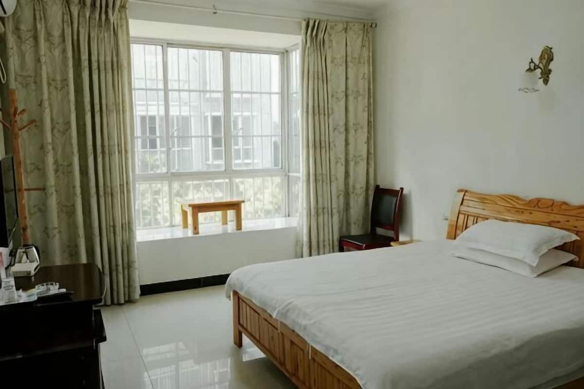 Une chambre à coucher comprenant un lit, une tête de lit en bois, une table de chevet, un téléviseur et une fenêtre avec des rideaux.