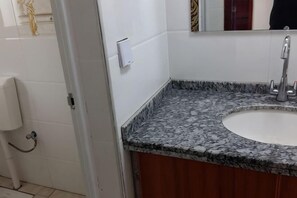 A bathroom with a marble sink, a mirror, and a toilet paper holder.