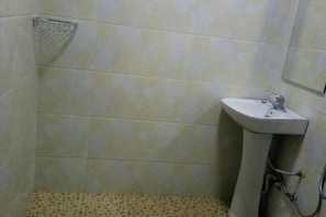 Un baño con piso de baldosas, un lavamanos pedestal y zona de ducha.