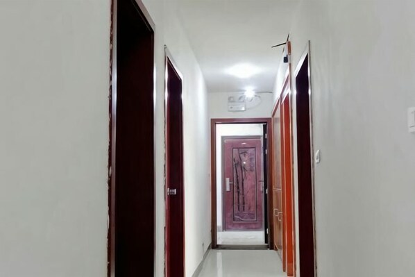 Un couloir étroit, avec des portes fermées, un luminaire au plafond et une porte au bout.