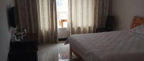 A hotel room with a bed, a wooden headboard, a desk with a chair, and a television on the wall.