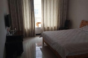 Una habitación de hotel con una cama, cabecera de madera, un escritorio con una silla y un televisor en la pared.