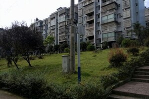 Un immeuble résidentiel à plusieurs étages doté de balcons, d’un espace verdoyant agrémenté d’arbustes et d’un chemin menant à l’entrée.
