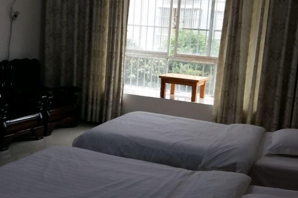 A room with two beds, a wooden table, and a window with curtains.