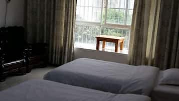 Ein Zimmer mit zwei Betten, einem Holztisch und einem Fenster mit Vorhängen.