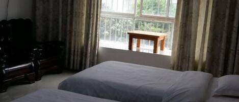 A room with two beds, a wooden table, and a window with curtains.