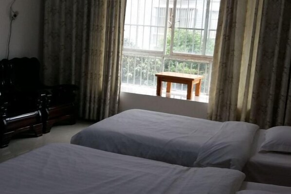 A room with two beds, a wooden table, and a window with curtains.