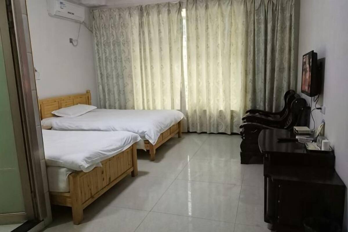 Une chambre d’hôtel avec deux lits en bois, un bureau avec une chaise, une télévision et une fenêtre avec des rideaux.