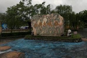 A stone monument with inscriptions, surrounded by a paved area with a panda statue and a small garden. - Qingya Inn on the West Grand Canyon Hot Spring (Shuifu)