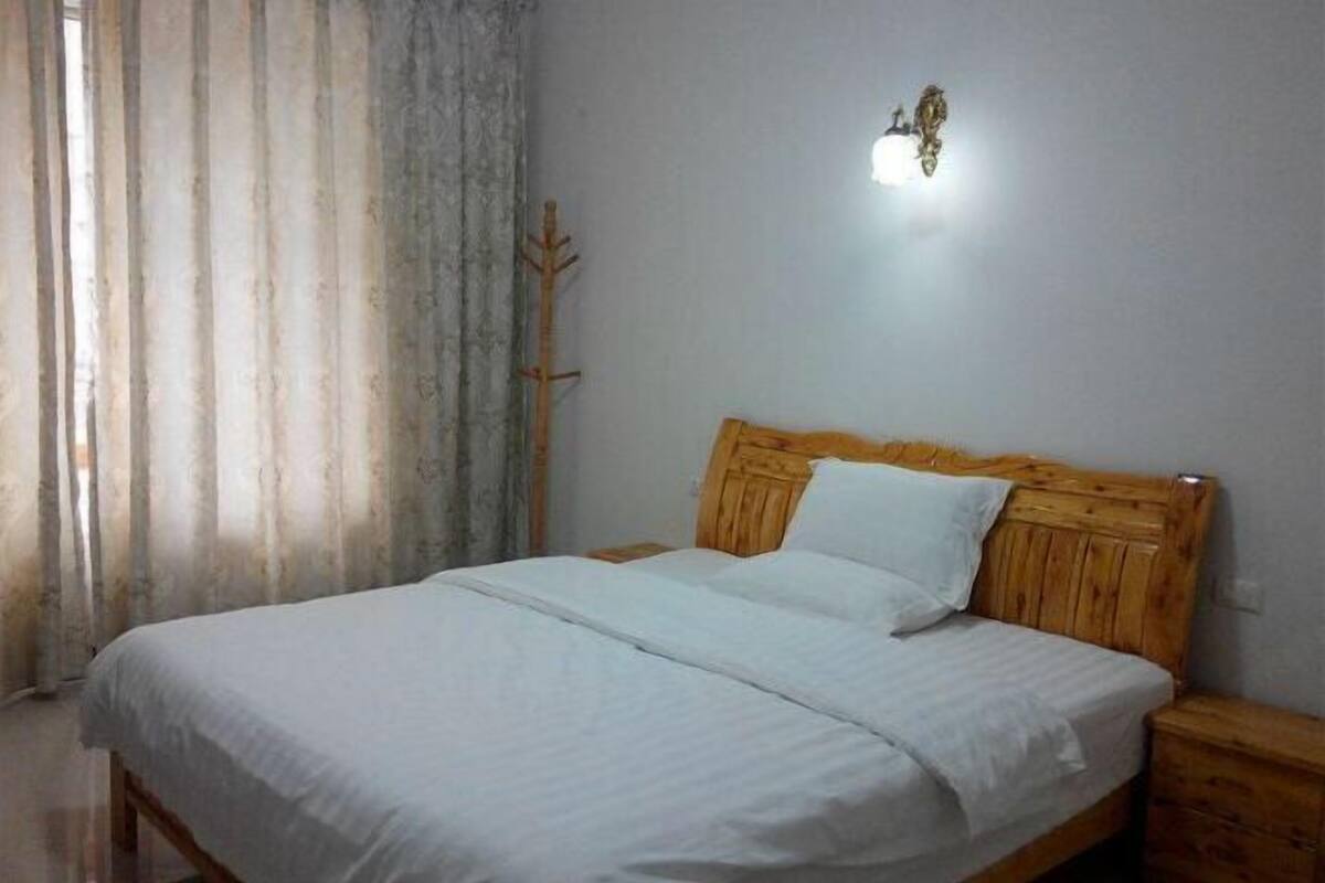 Une chambre à coucher avec un lit en bois, une literie blanche, une table de chevet et un luminaire fixé au mur.