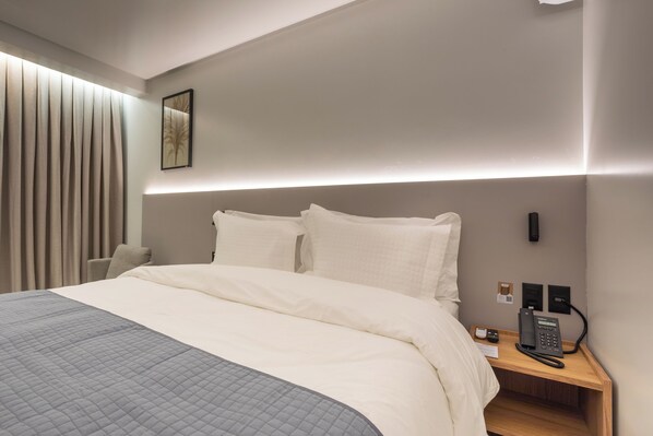 Una habitación de hotel moderna con una cama grande, una mesita de noche con teléfono, y un aplique de pared.