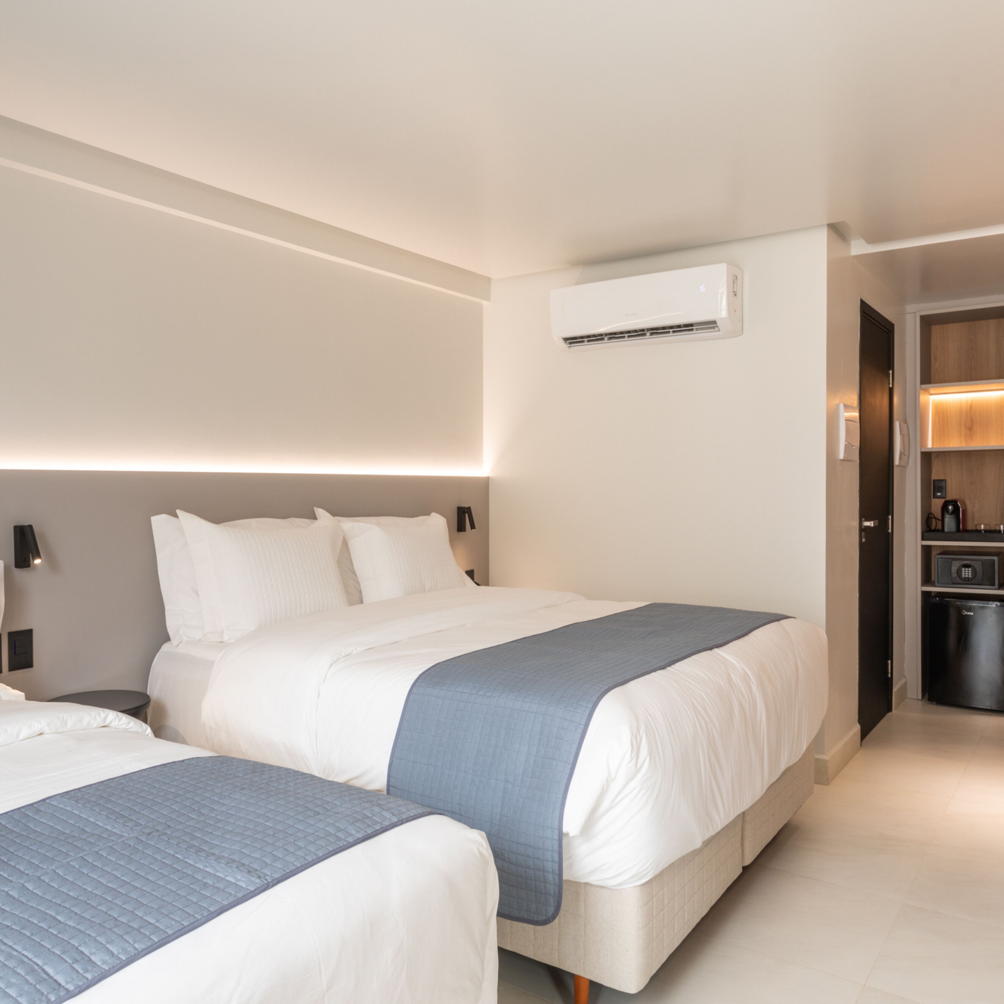 A modern hotel room with a large bed, a smaller bed, and a built-in air conditioning unit.