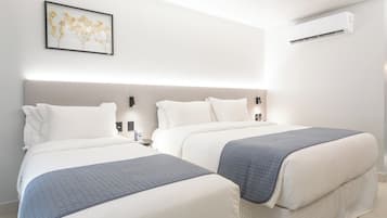 Quarto de hotel com duas camas, uma pintura floral emoldurada na parede e um aparelho de ar condicionado.