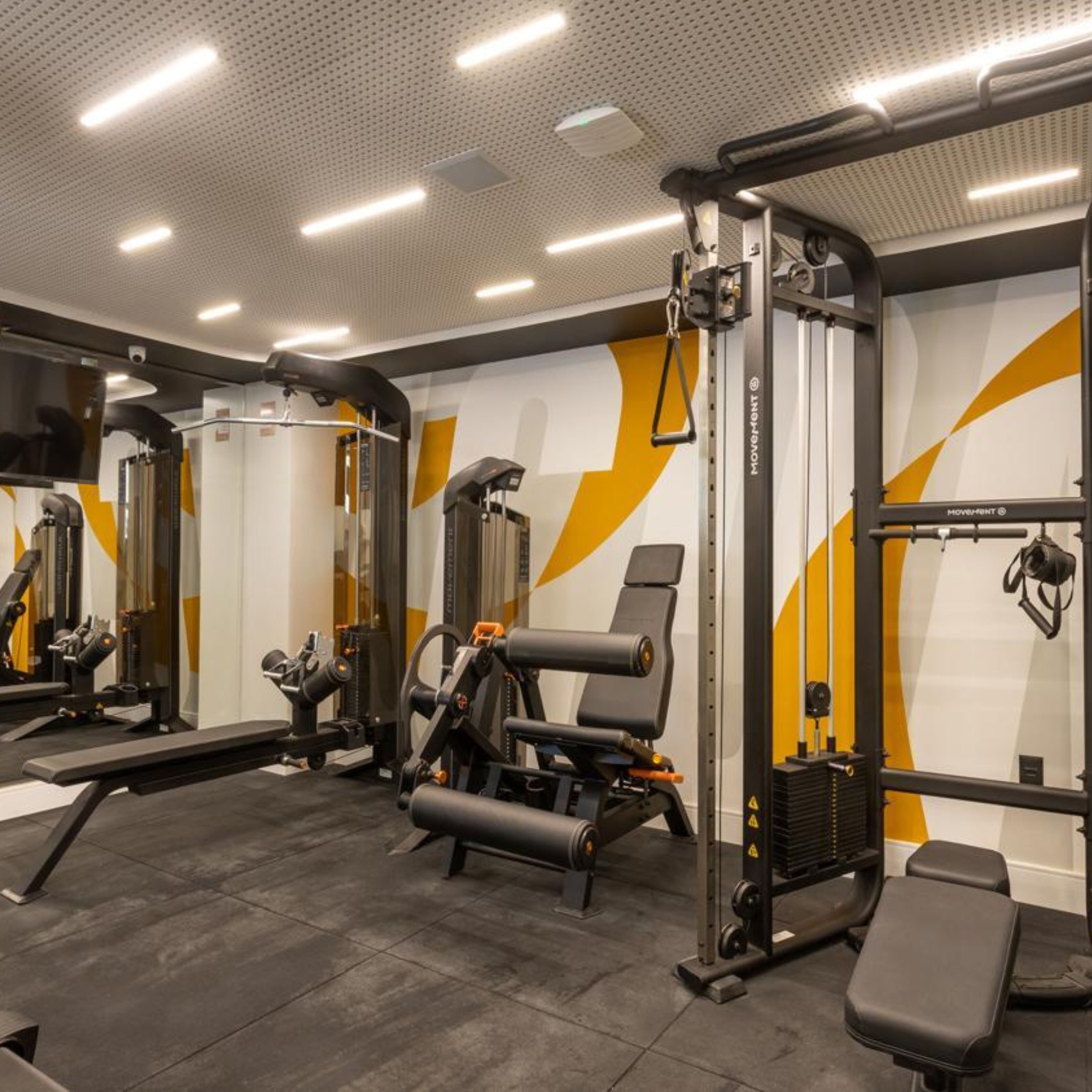 Un gimnasio con diferentes máquinas de ejercicio, espejos y un banco.
