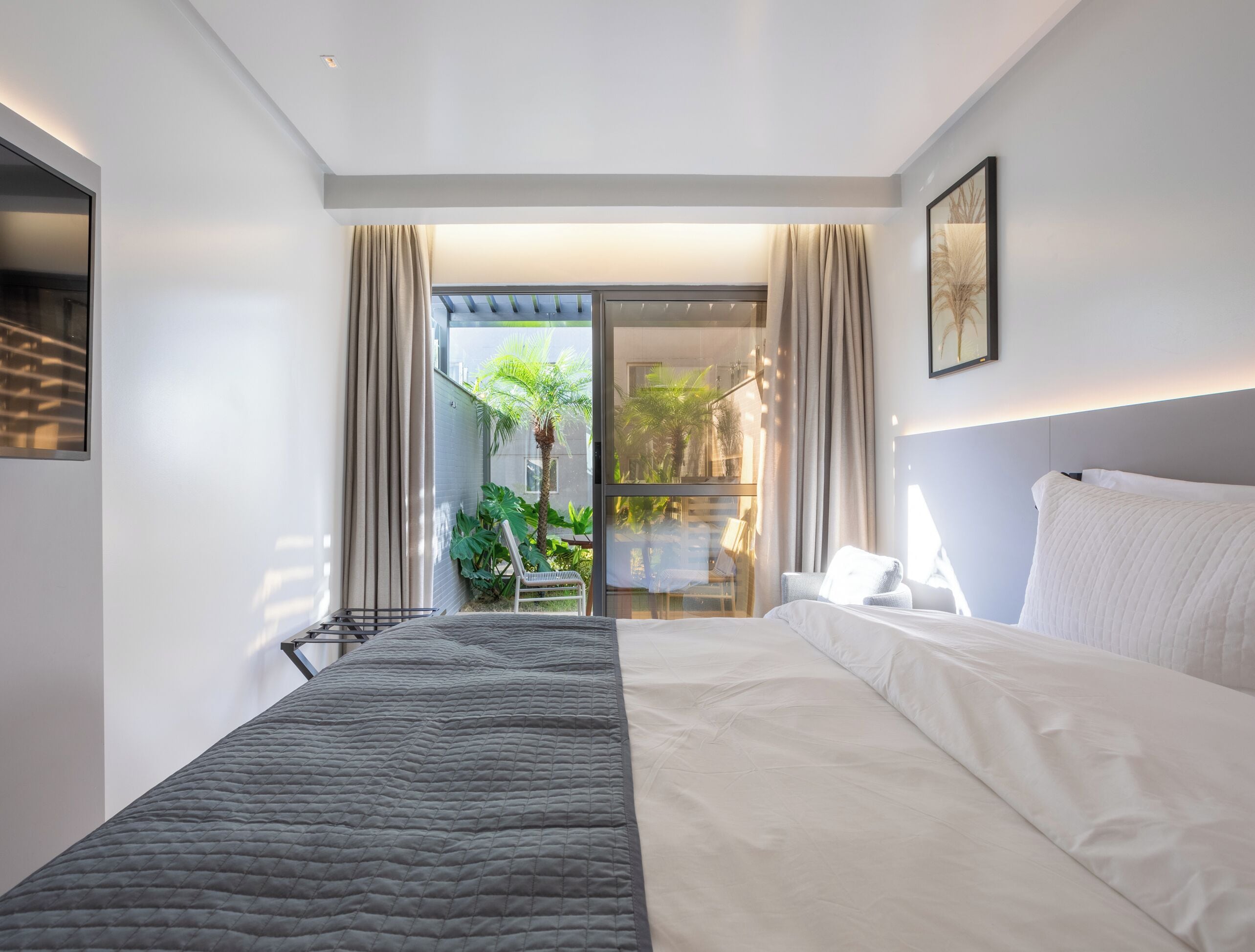 Una habitación de hotel moderna con una cama grande, vistas al exterior y un balcón con cortinas.