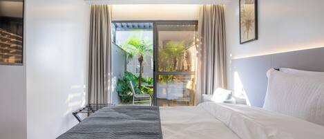 Una habitación de hotel moderna con una cama grande, vistas al exterior y un balcón con cortinas.